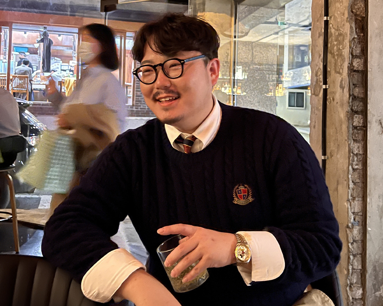 Cable knit sweater layered over an Oxford shirt and tie in Ivy style