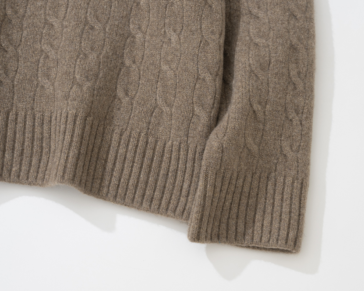 Close-up of Renacts cable knit sweater with crest and balanced cable pattern