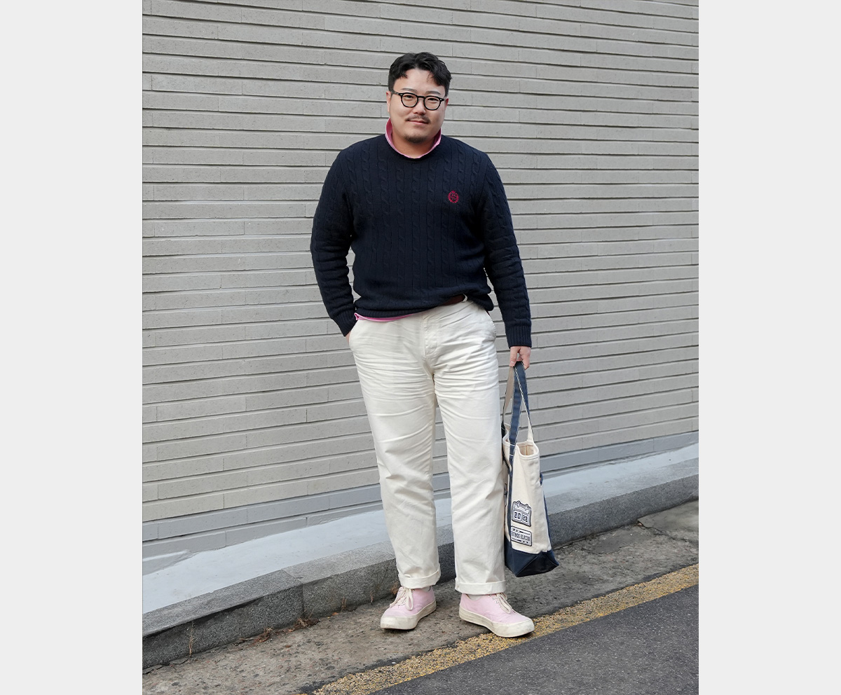 A man wearing a navy cable knit, white pants, and pink accent items.