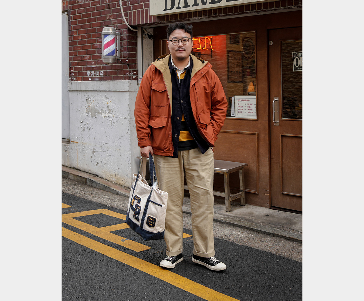 Street fashion of a man layering an orange mountain parka over a corduroy jacket.