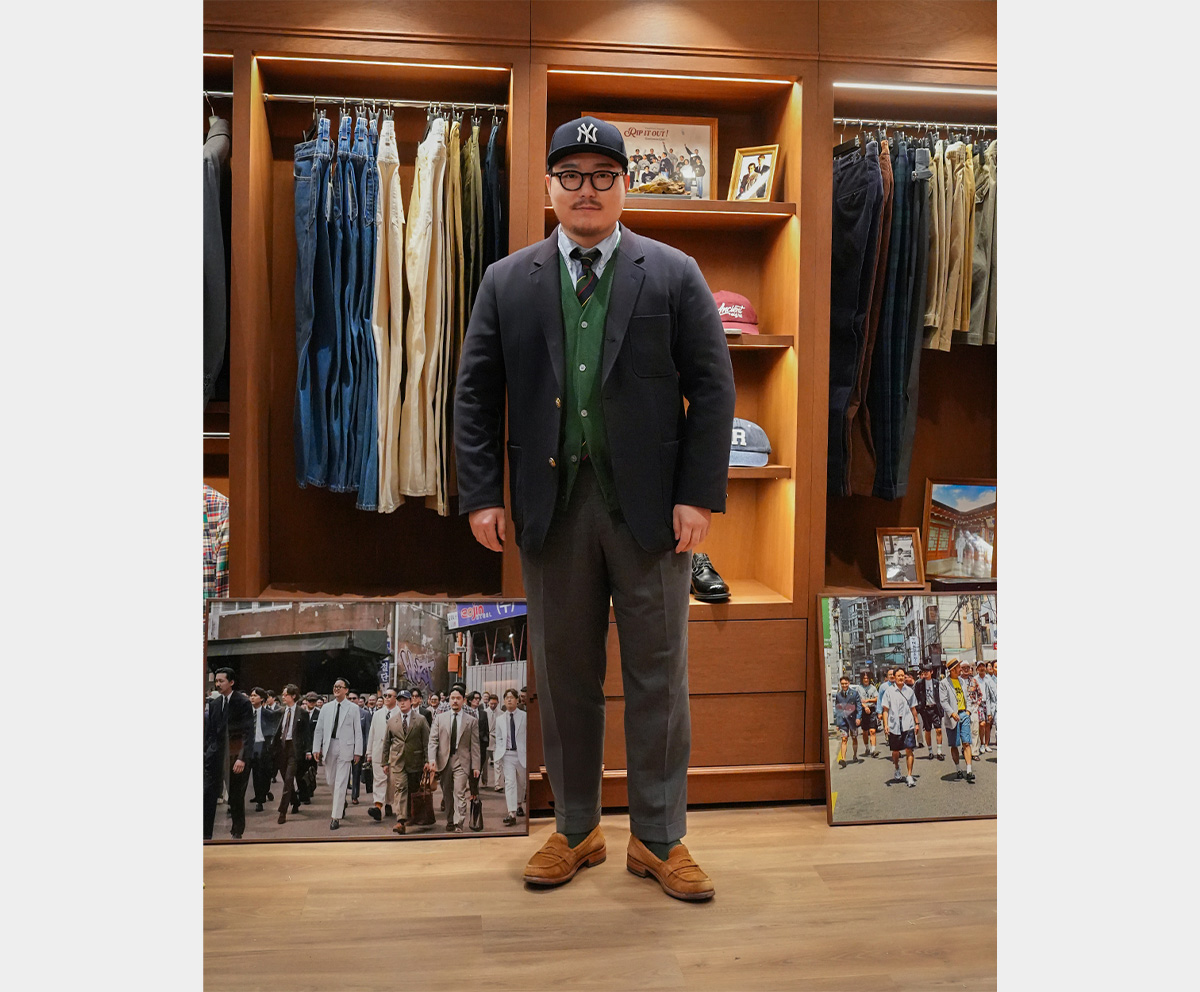 Full-body photo of a man wearing a navy blazer, gray trousers, and a ball cap.