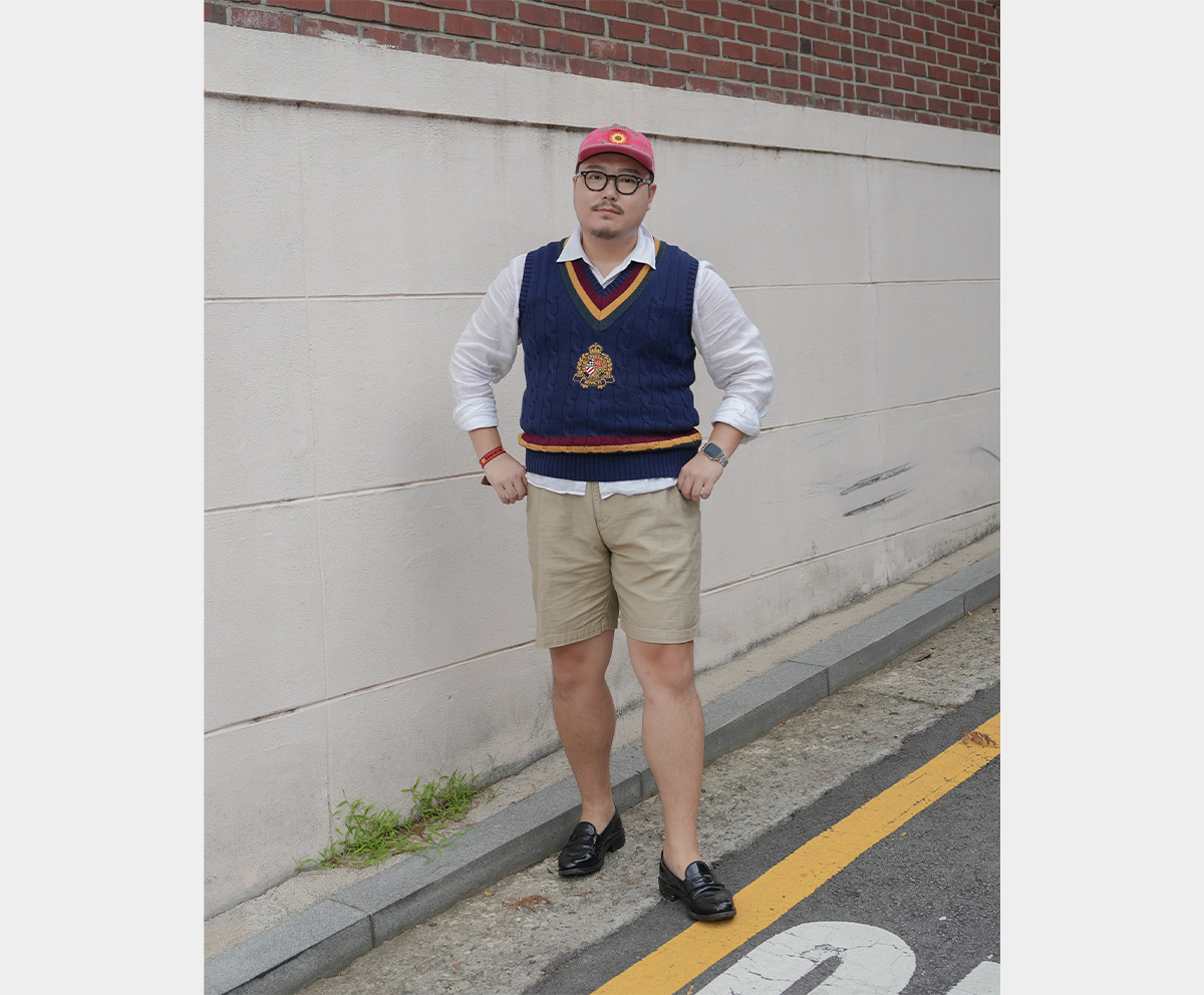 Full-body photo of a man posing in a cricket knit vest and beige shorts.