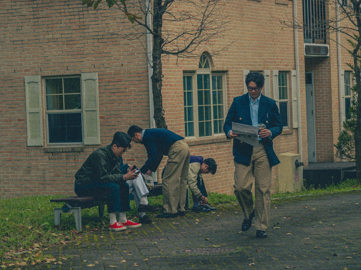 A young man in a navy blazer and repp stripe tie, photographed on a college campus in the early 1960s