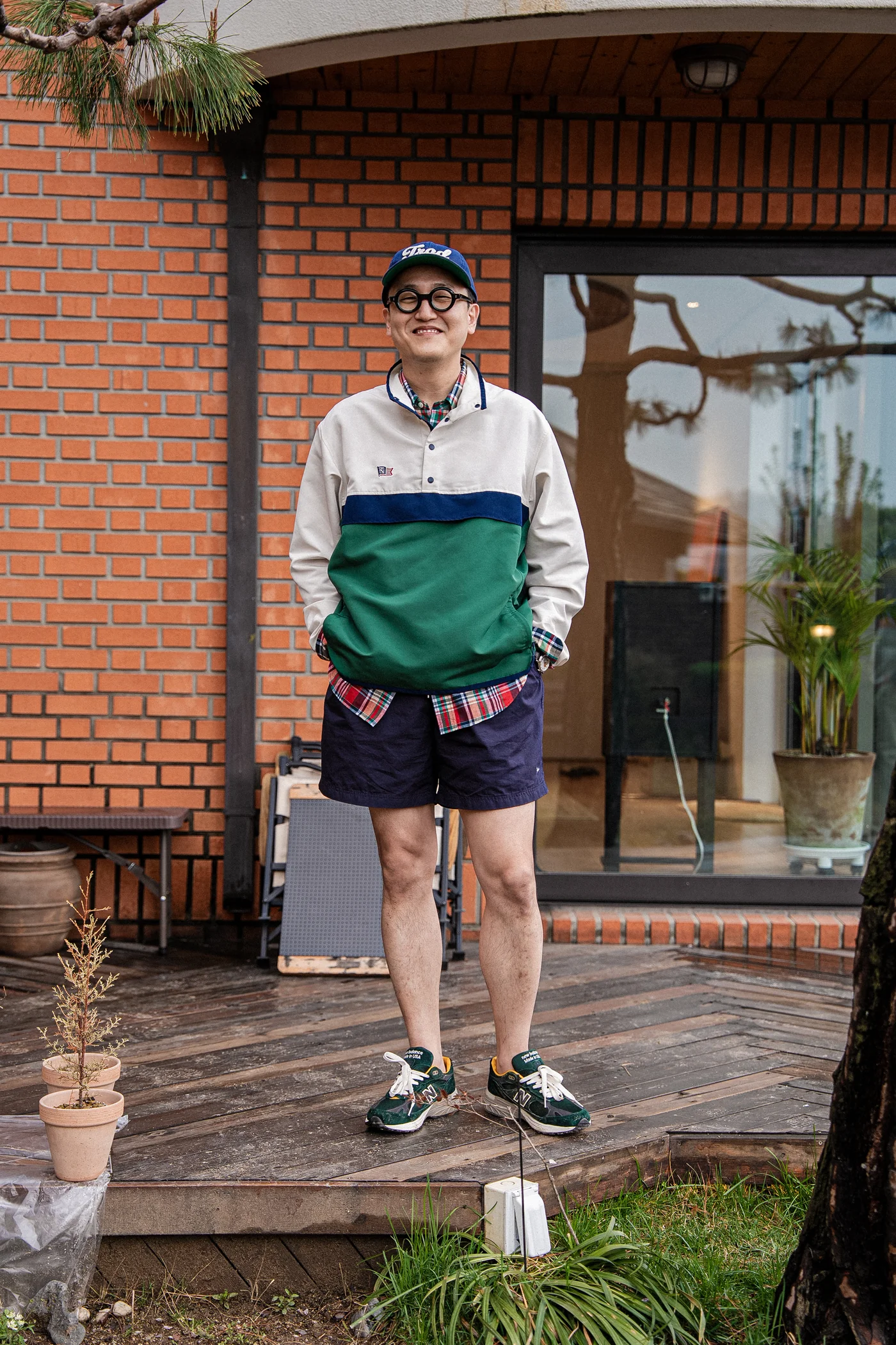 Anorak outfit men spring — Renacts anorak over madras shirt with nylon shorts, New Balance 993 Aimé Leon Dore collab sneakers, ballcap