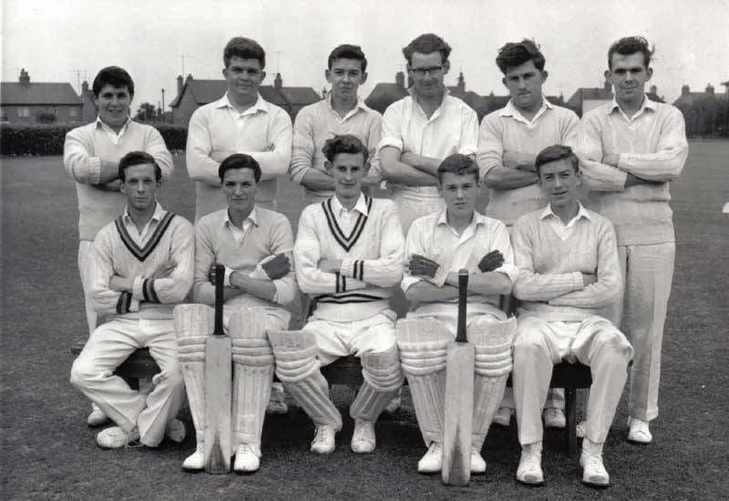 Cricket sweater heritage: a mid-20th century cricket team in classic V-neck cable-knit cricket sweaters with striped tipping, cricket whites, pads, and bats — the sweater in its natural habitat