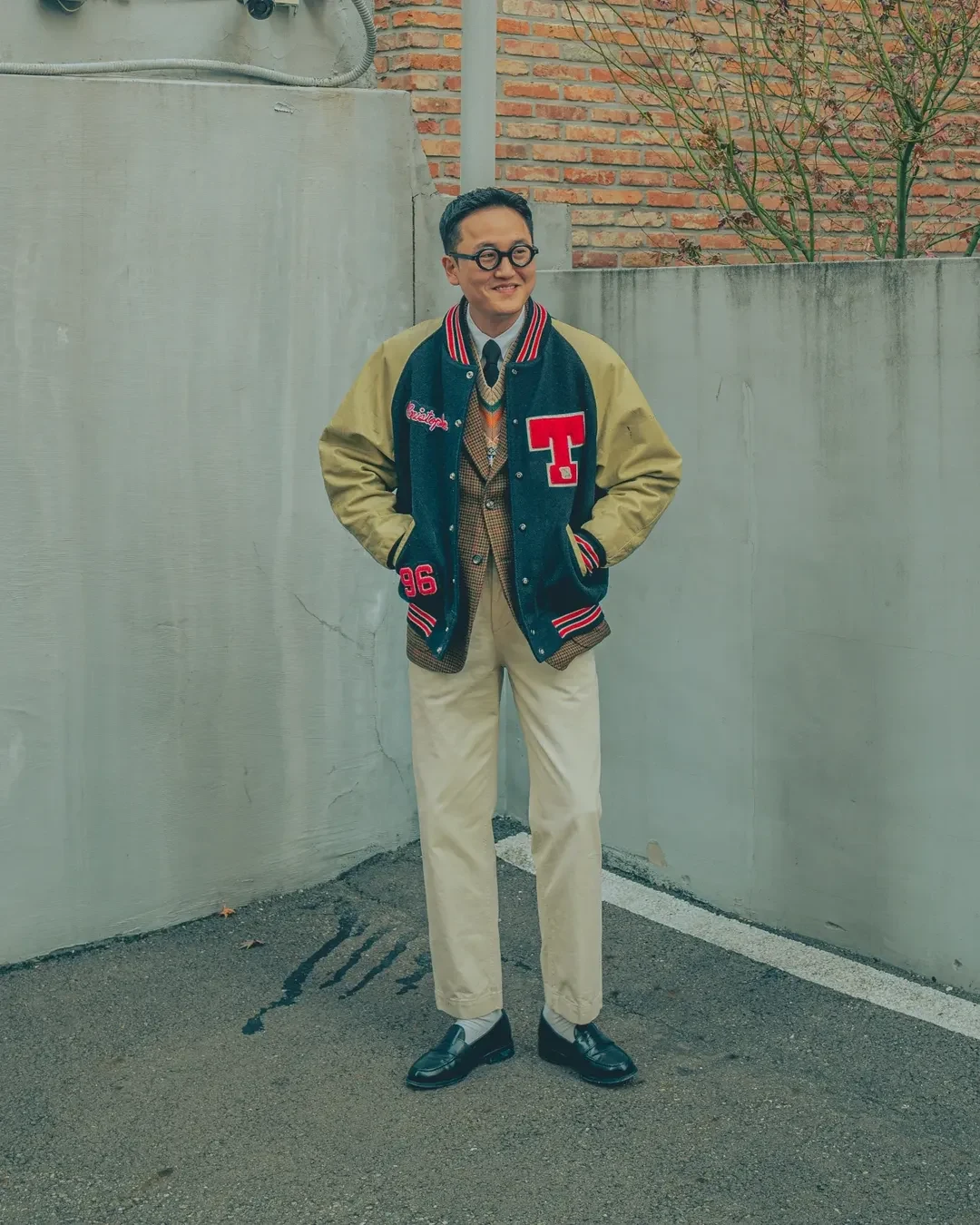 How to wear a Fair Isle vest with a knit tie: black knit tie under a Gun Club sport coat under a varsity jacket, layered over Fair Isle vest, with ivory chinos and black penny loafers