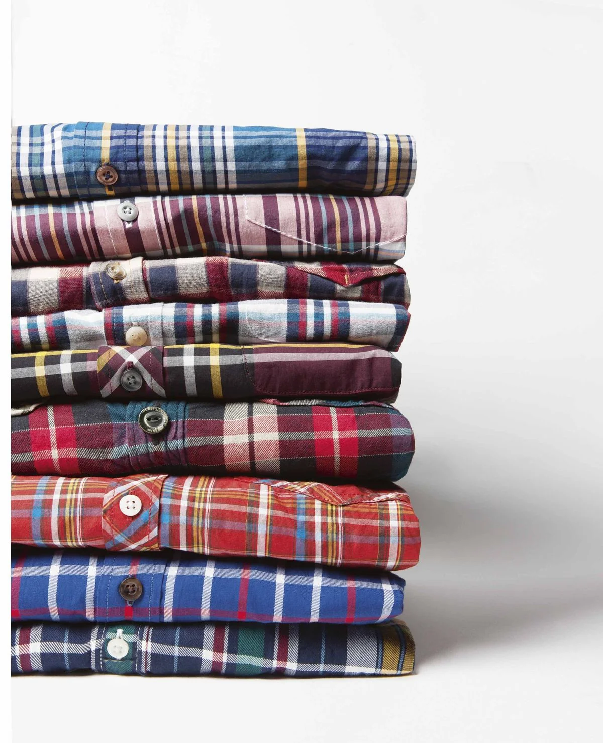 How to wear madras shirt — vertical stack of nine folded madras shirts showing pattern and color range