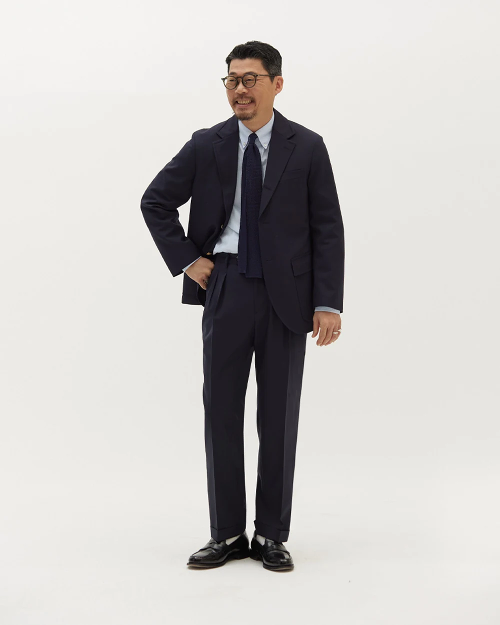 Navy gold-button blazer outfit — single-breasted blazer, white OCBD, black silk knit tie, navy wool slacks, plaque belt, black penny loafers, evening register configuration