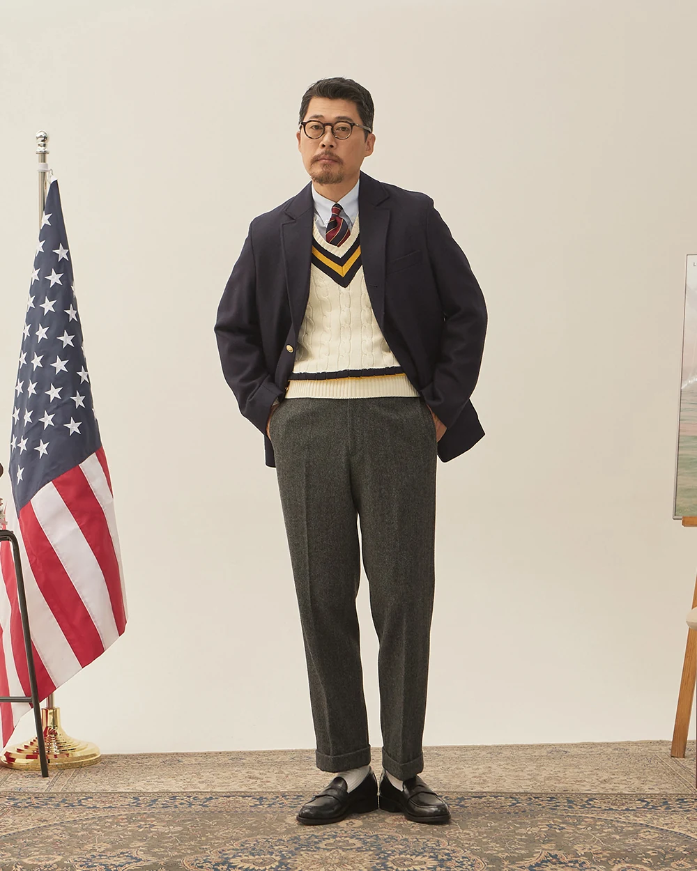 Navy gold-button blazer outfit with cricket sweater — single-breasted blazer over cricket sweater, white OCBD, regimental rep tie, charcoal grey wool slacks, plaque belt, black penny loafers