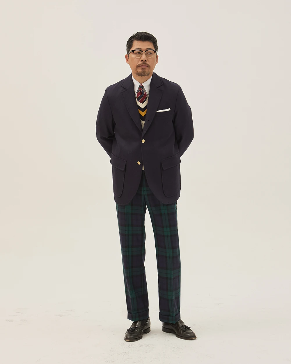Navy gold-button blazer outfit with cricket sweater — blazer over cricket, white OCBD, regimental rep tie, Blackwatch tartan wool slacks, plaque belt, black tassel loafers, holiday season configuration