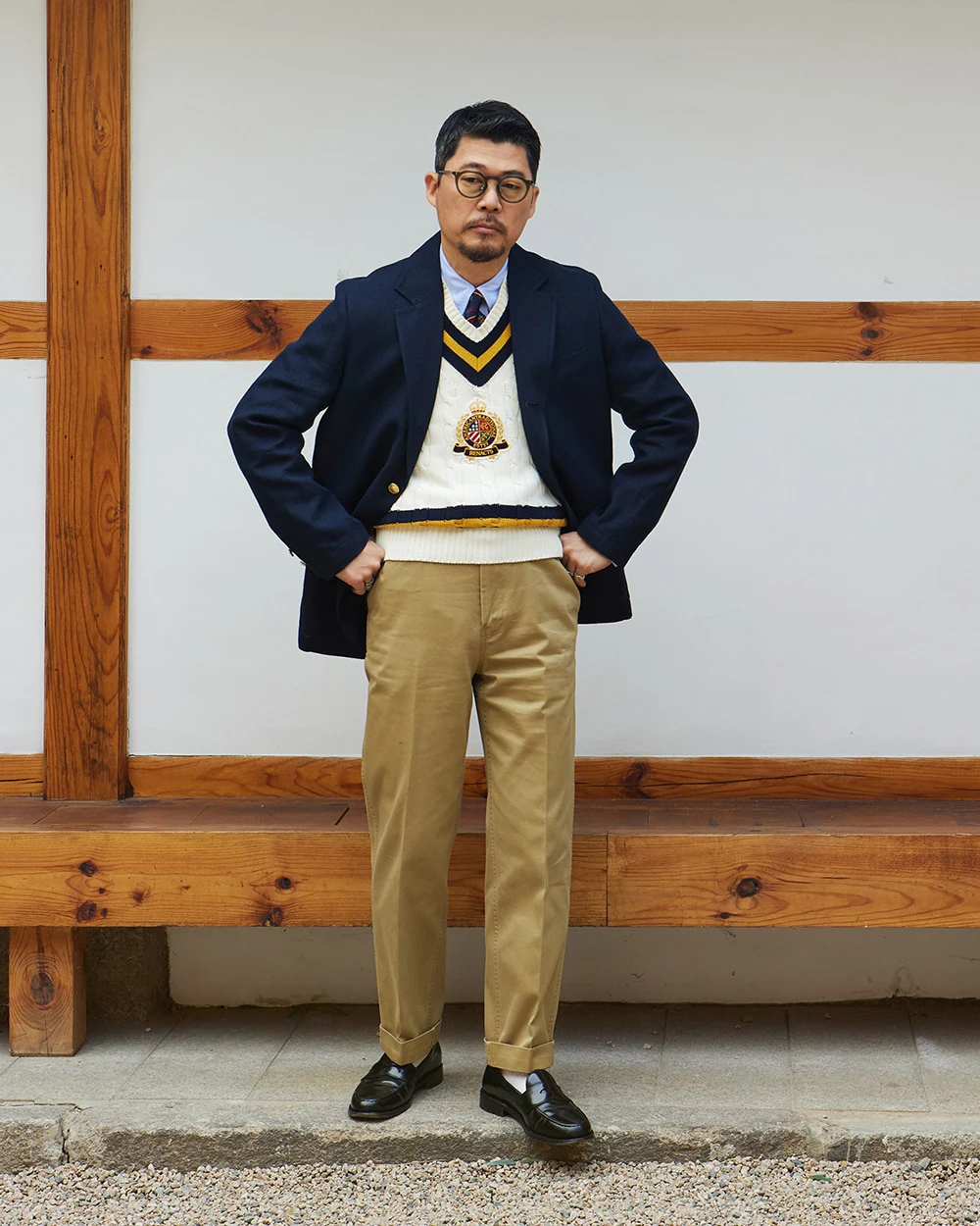 Navy gold-button blazer outfit with cricket sweater vest — single-breasted blazer over cricket V-neck vest, white OCBD, regimental rep tie, khaki chinos, plaque belt, black penny loafers
