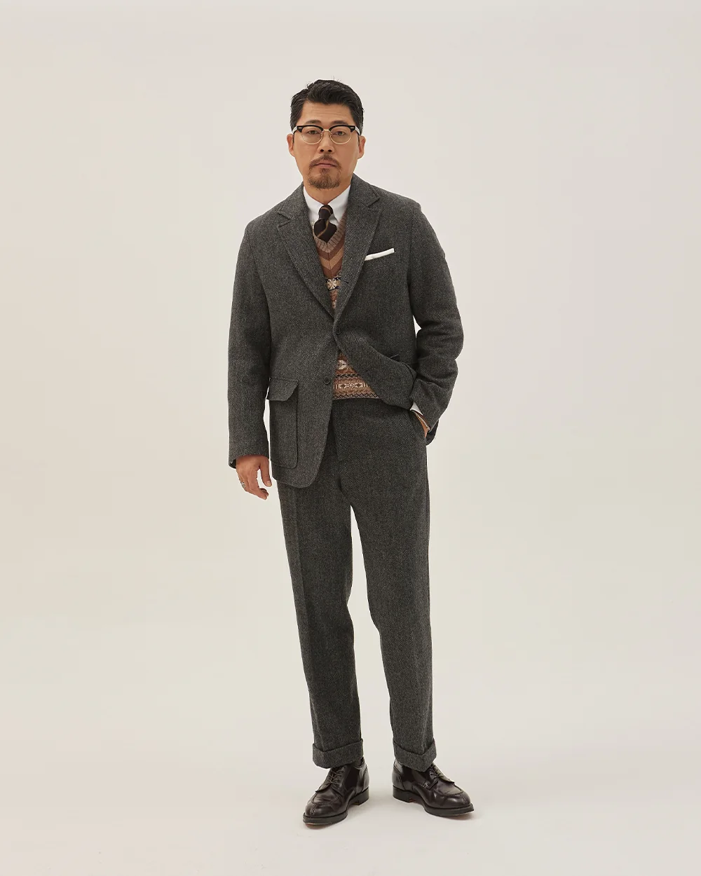 How to wear a Fair Isle vest in Seoul Traditional style: charcoal grey tweed wool sack suit over Fair Isle vest layered with white oxford button-down and regimental rep tie, black plain-toe derbies — full Heavy Ivy autumn outfit