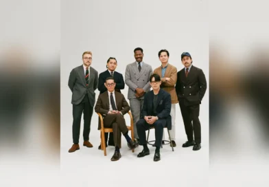 Drake's of London History — group portrait of Drake's customers in suits, sport coats, and regimental ties, photographed in studio (the full ready-to-wear program after the 2013 Rayner & Sturges acquisition)