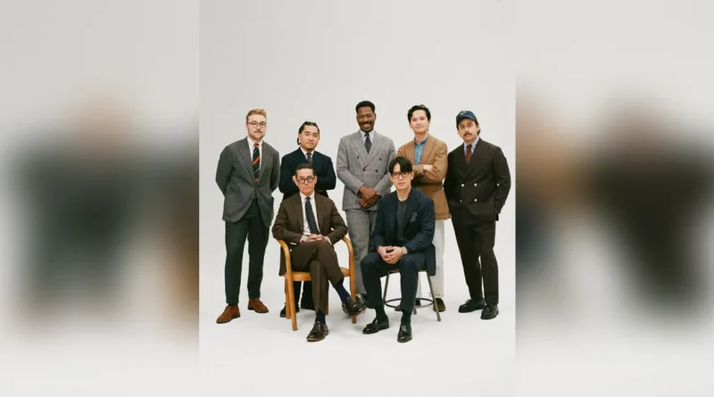 Drake's of London History — group portrait of Drake's customers in suits, sport coats, and regimental ties, photographed in studio (the full ready-to-wear program after the 2013 Rayner & Sturges acquisition)