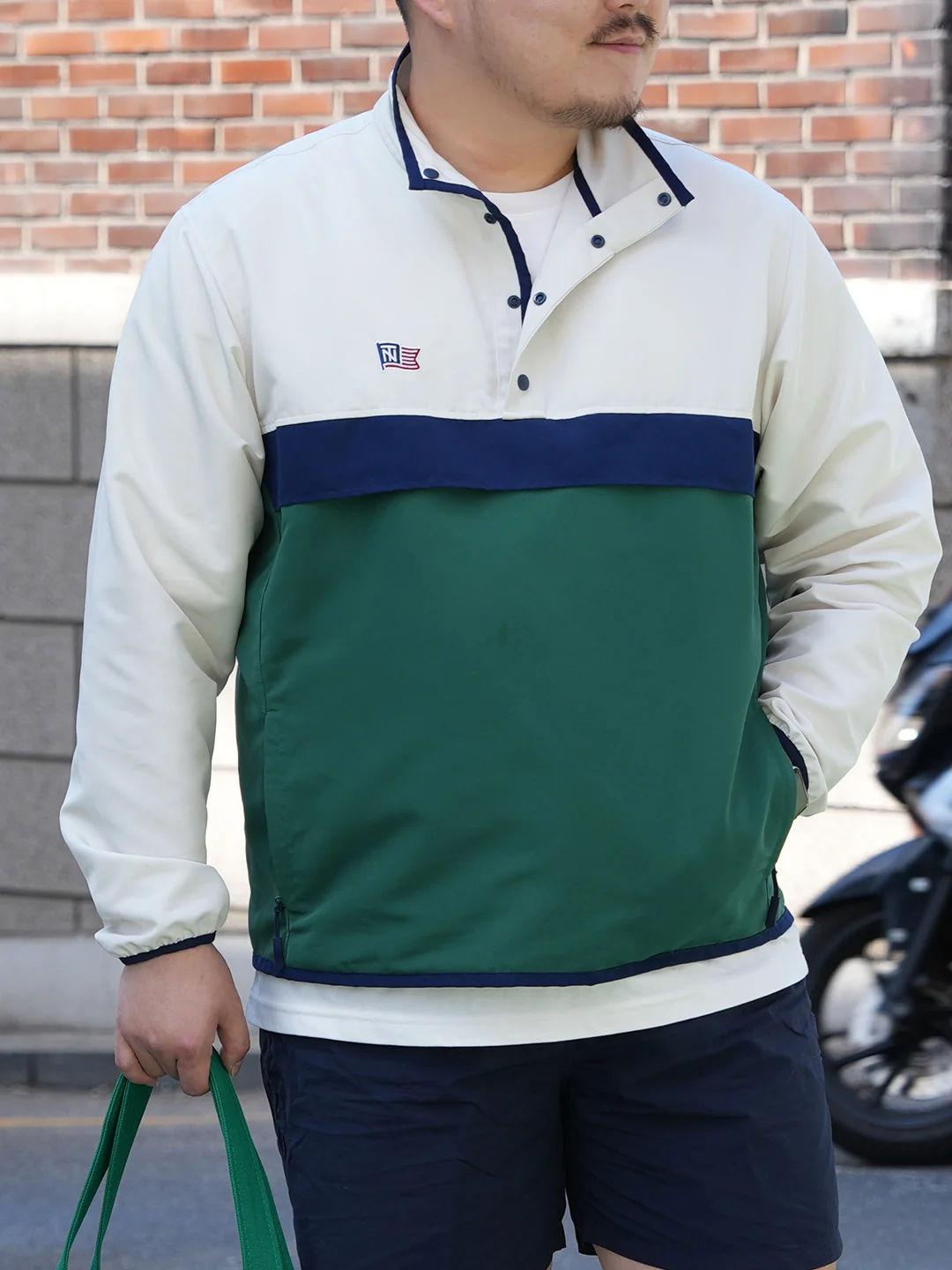 Bicolor anorak detail — ivory upper, navy chest stripe, green body, snap-button placket collar, Renacts N flag patch on the chest