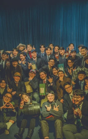 Gentlemens Club Seoul Vol. 6 group photograph — fifty members holding Wild Turkey bottles and boxes in front of a deep-blue curtain