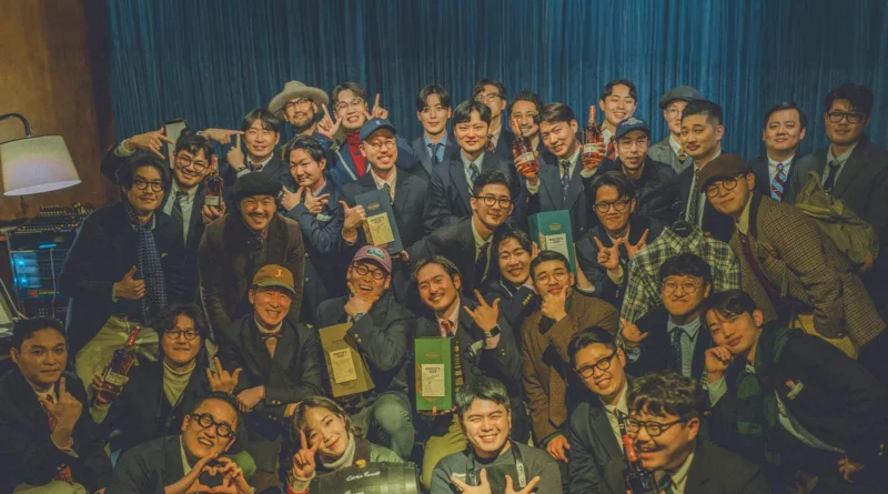 Gentlemens Club Seoul Vol. 6 group photograph — fifty members holding Wild Turkey bottles and boxes in front of a deep-blue curtain