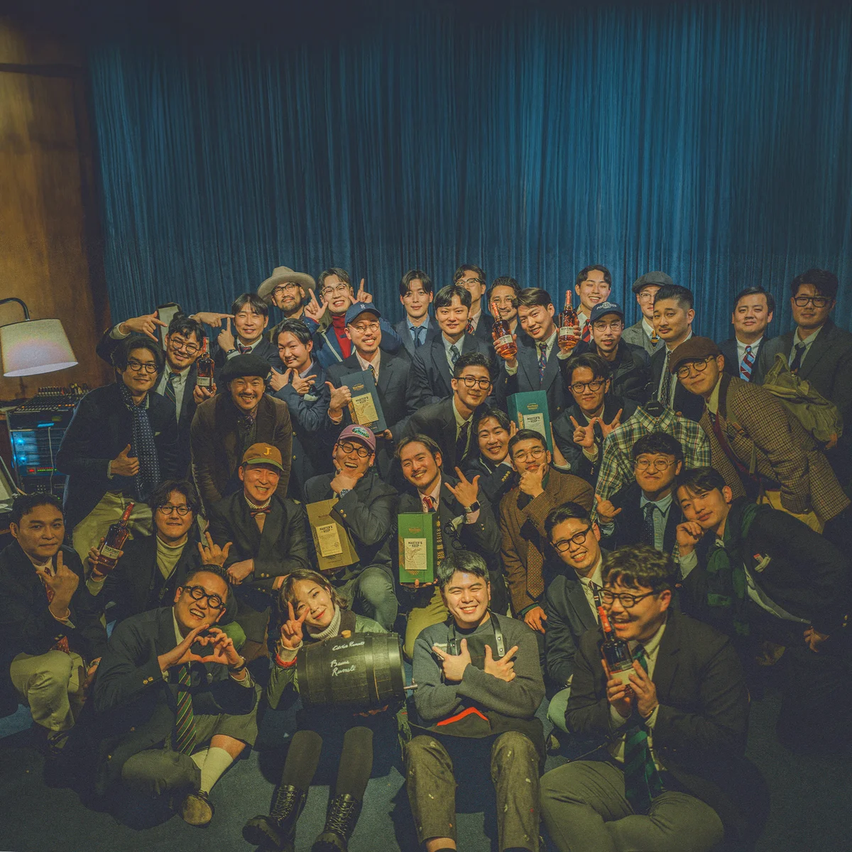 Gentlemens Club Seoul Vol. 6 group photograph — fifty members holding Wild Turkey bottles and boxes in front of a deep-blue curtain