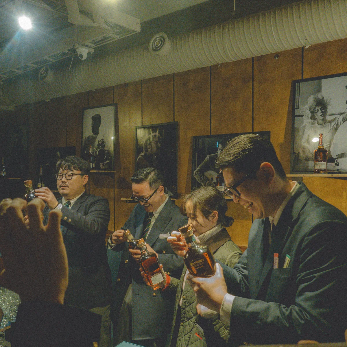 Wild Turkey tasting in detail — members holding bottles up to study color and aroma, framed black-and-white portraits behind