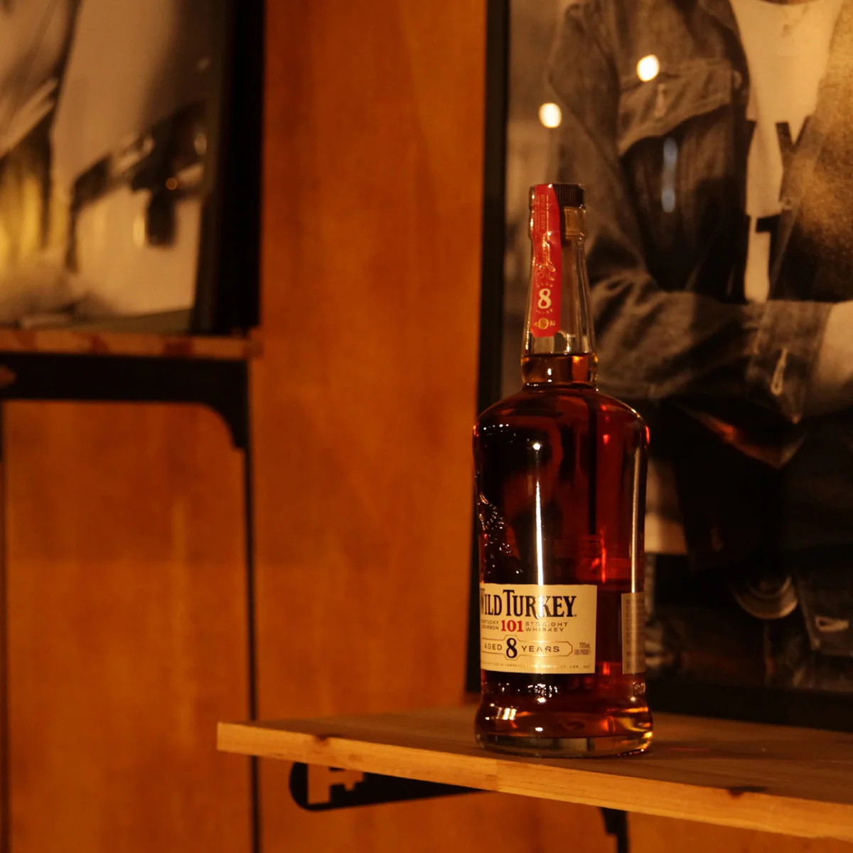 Wild Turkey 101 eight-year bottle still life — black-and-white portrait behind, wood paneling lit warmly