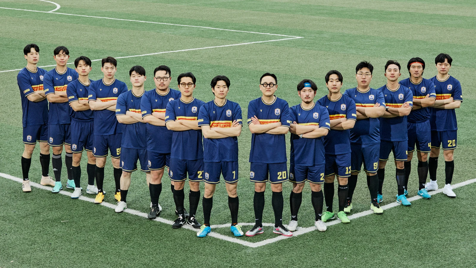 Gentlemens Football Club jersey row standing: sixteen members in navy GENTLEMENS football kits arms crossed standing in single line on the centre line at Guri Wangsuk after the match