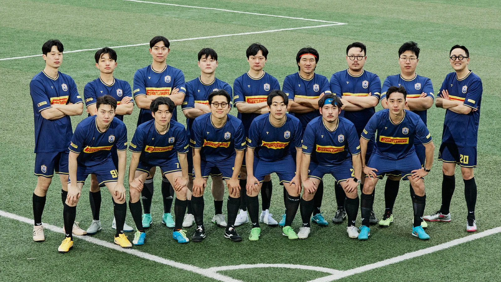 Gentlemens Football Club official team photo: sixteen members in navy GENTLEMENS jerseys two-row formation kneeling front row and standing back row at Guri Wangsuk Sports Park artificial turf