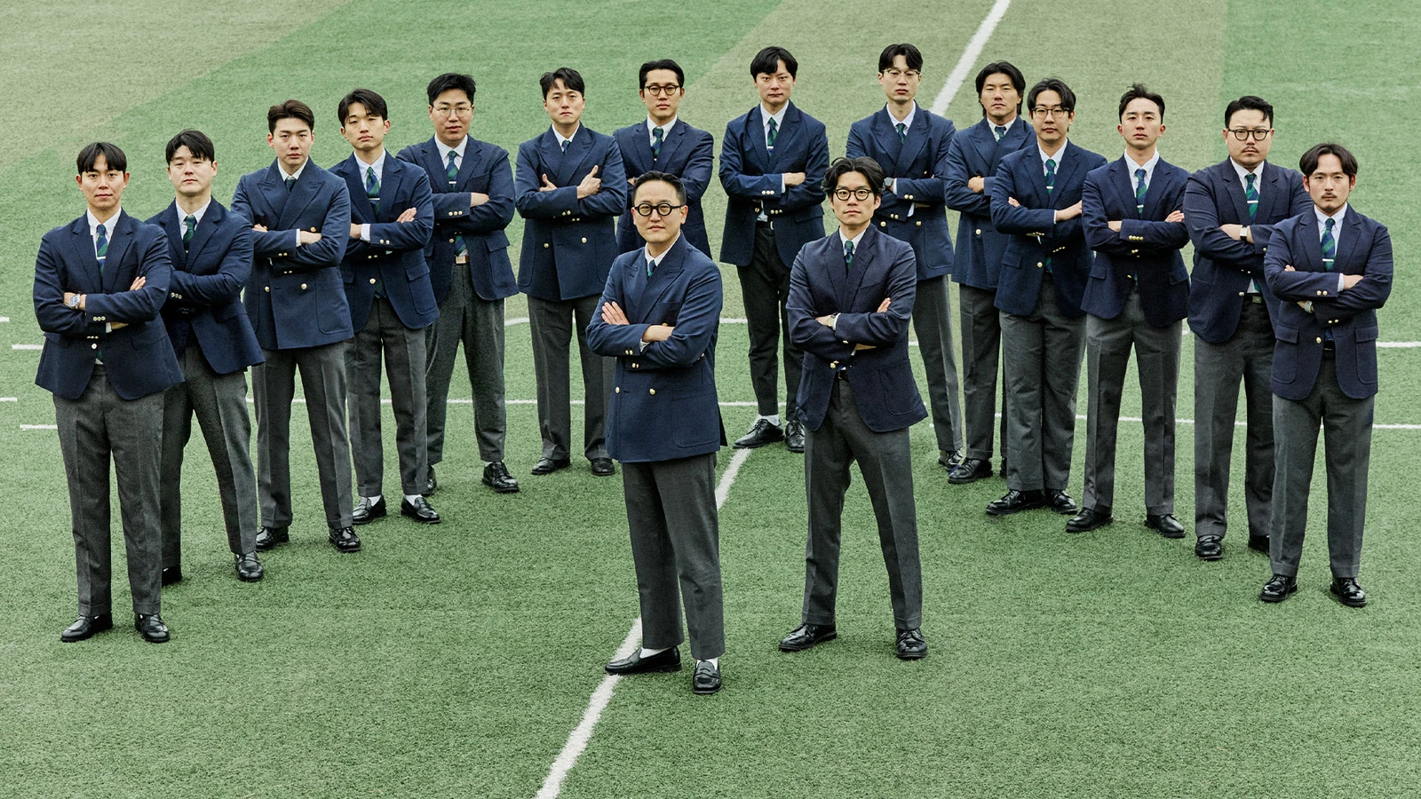 Gentlemens Football Club team suits lineup: sixteen members in navy gold-button blazers single and double-breasted with grey wool trousers arms crossed standing on the centre line at Guri Wangsuk Sports Park