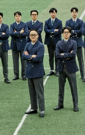 Gentlemens Football Club Sound Mind Sound Body thumbnail: sixteen members of the football club standing arms crossed in navy gold-button single and double-breasted blazers grey wool pipe stem trousers and regimental ties on the centre line at Guri Wangsuk Sports Park — captain Lee Tae-yeol at front centre