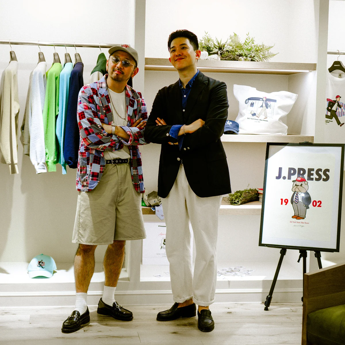 Aaron Chang and Tomoya Kurono together at the J.Press × Aaron Chang Sindang-dong pop-up, beside the collab sweatshirts and J.Press 1902 mascot illustration