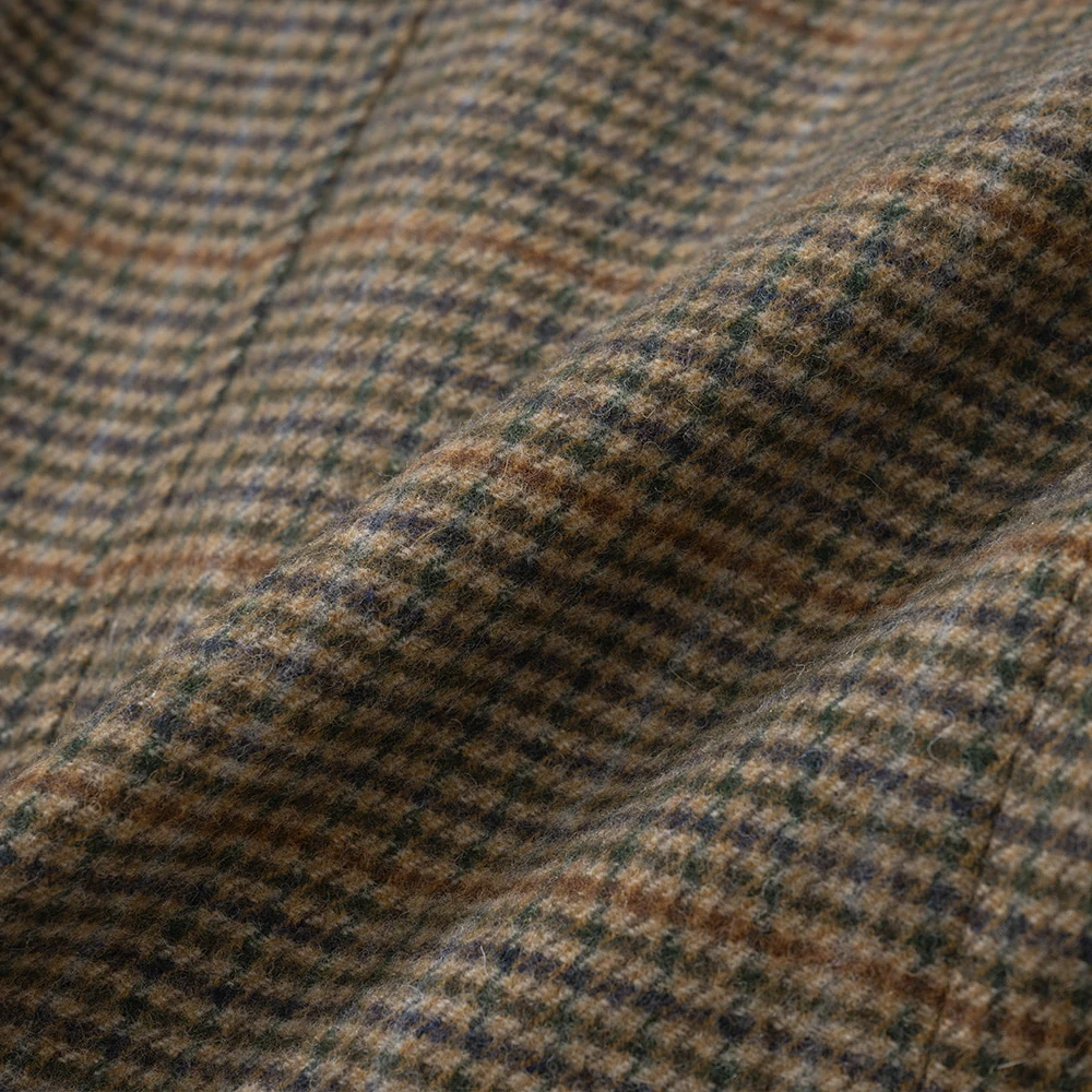Gun Club Check fabric close-up — four-color overcheck (olive, brown, rust, cream) on tweed base with subtle green windowpane