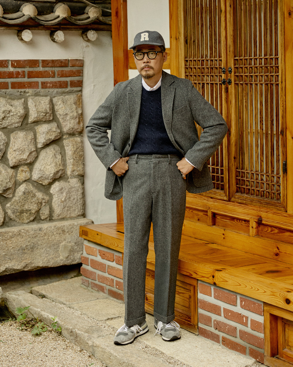 Grey herringbone sack jacket layered over a navy cable crewneck sweater โ cold-weather casual blazer layering