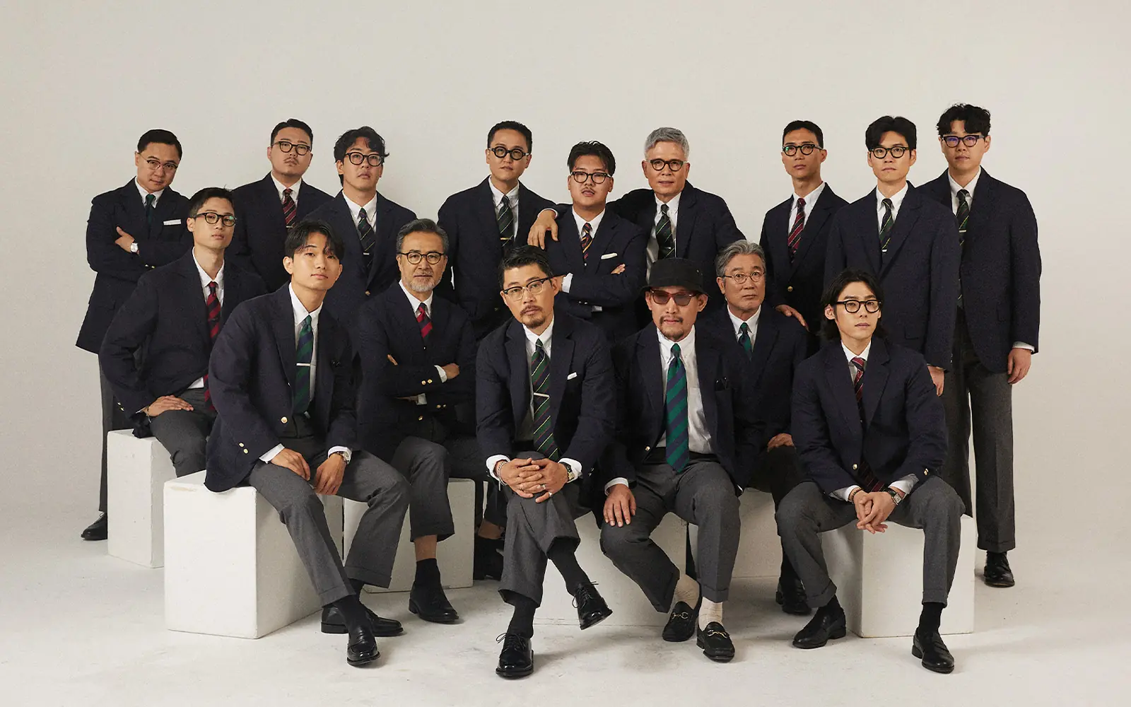 Fifteen men in navy blazers, grey flannel trousers and repp-striped ties, arranged in two rows against a plain studio backdrop.