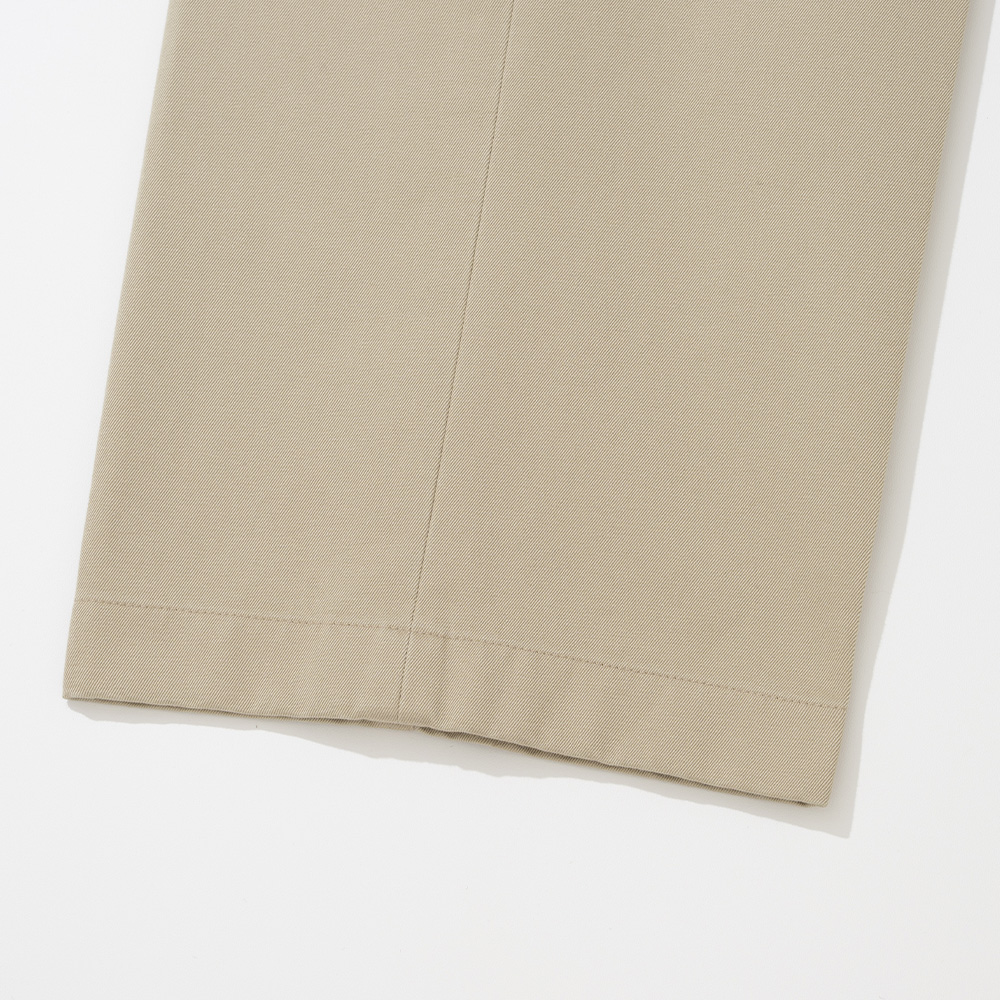 Close-up of a light beige chino hem showing the diagonal cotton twill weave and a plain turned hem