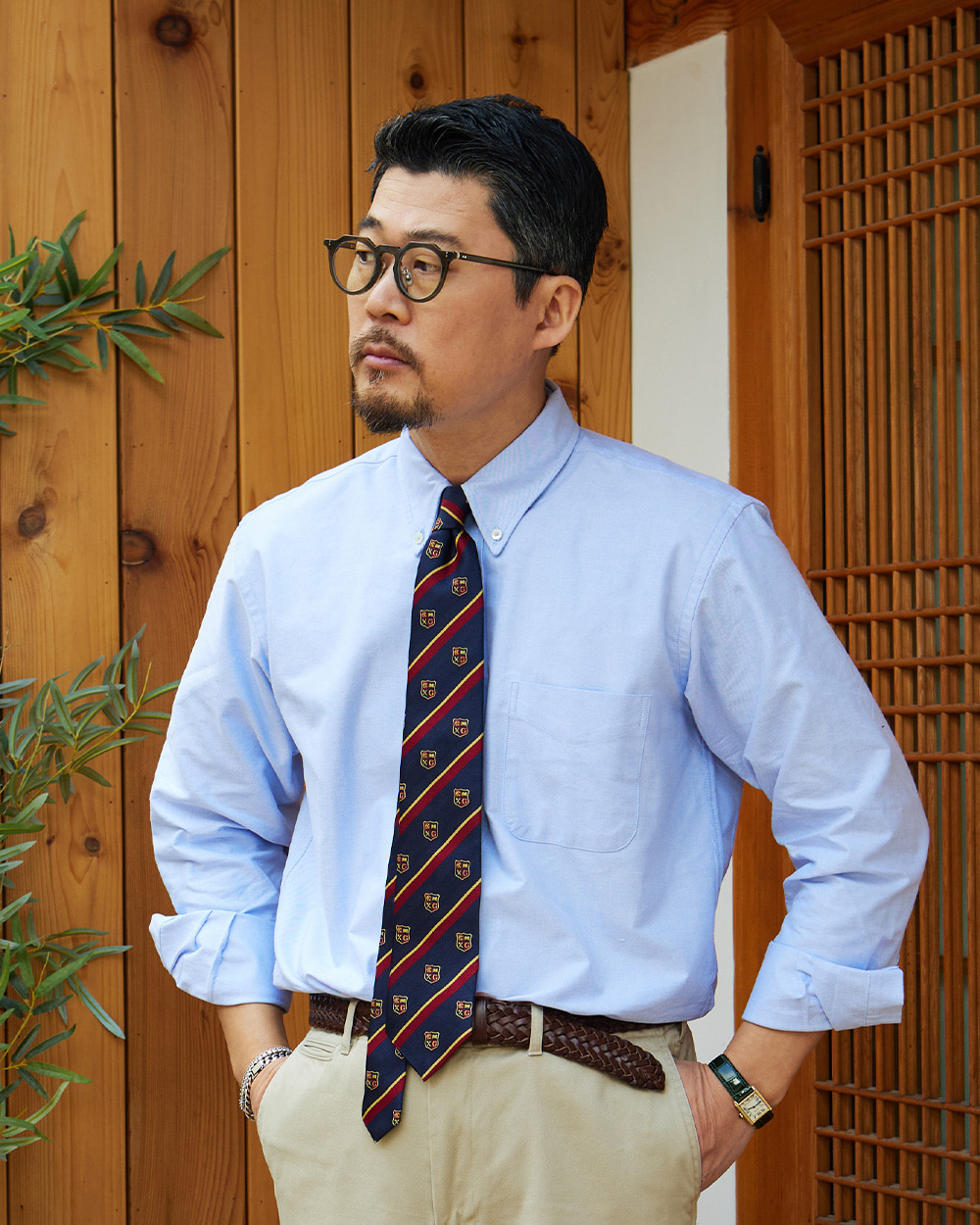 Light blue oxford cloth button-down collar rolling over a navy repp tie with a crest pattern, photographed in a hanok doorway in Seoul