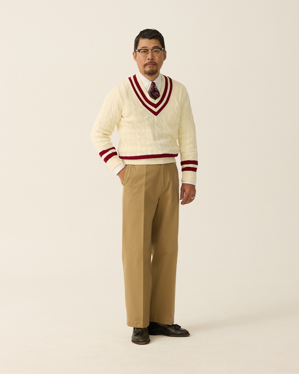 Ivory cable-knit cricket sweater with red and navy trim worn over a shirt and tie with khaki chinos and dark loafers