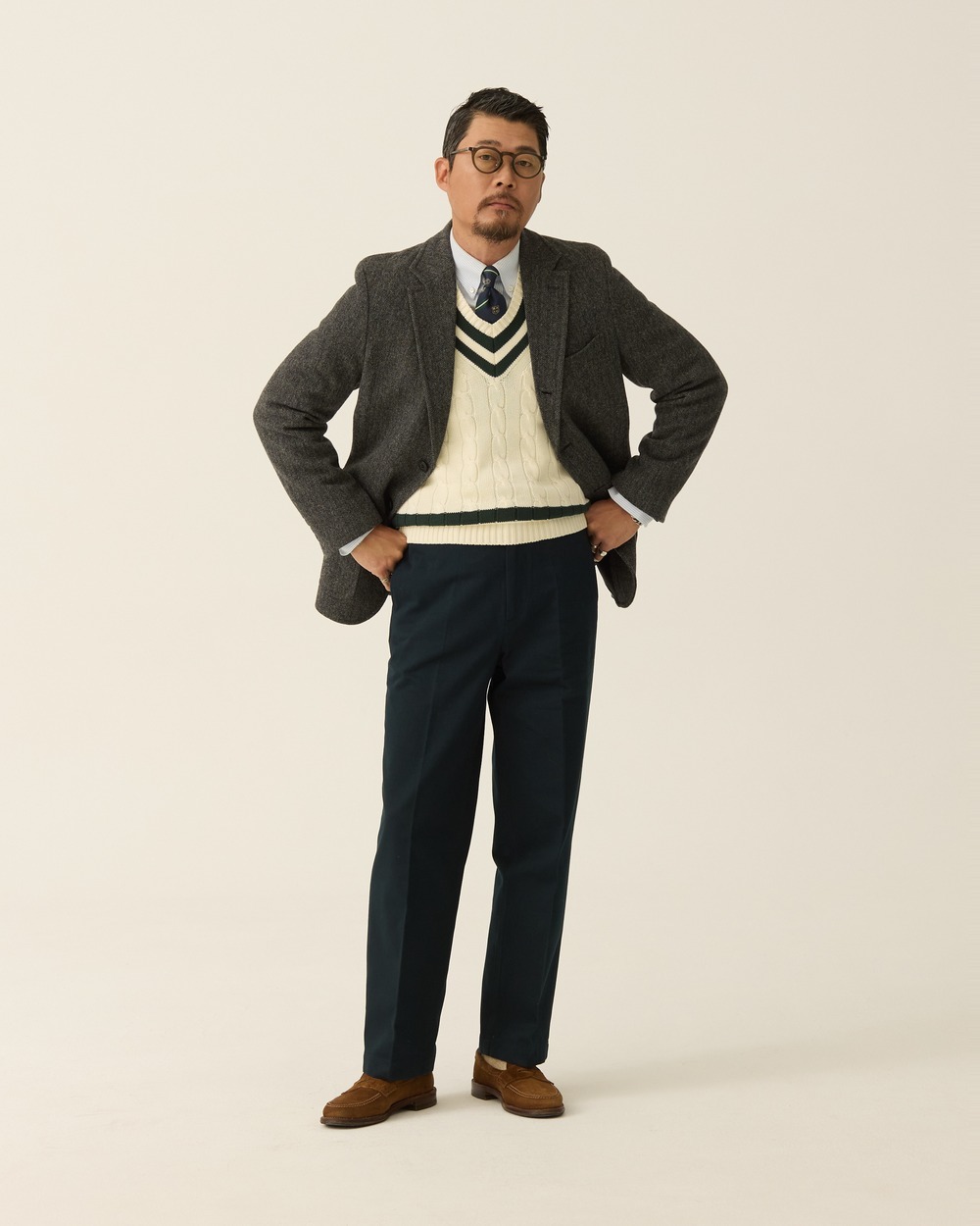 Brown tweed sport coat worn open over an ivory cricket sweater with green trim, a shirt and tie, navy trousers and brown suede loafers