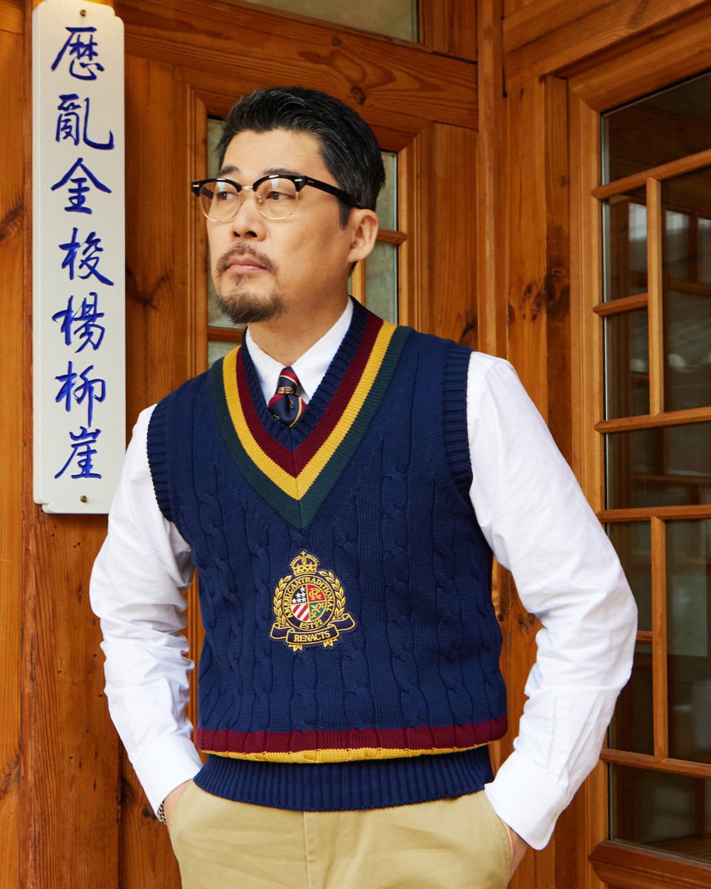 Navy crest cricket vest with red and gold trim worn over a white shirt and tie with khaki chinos