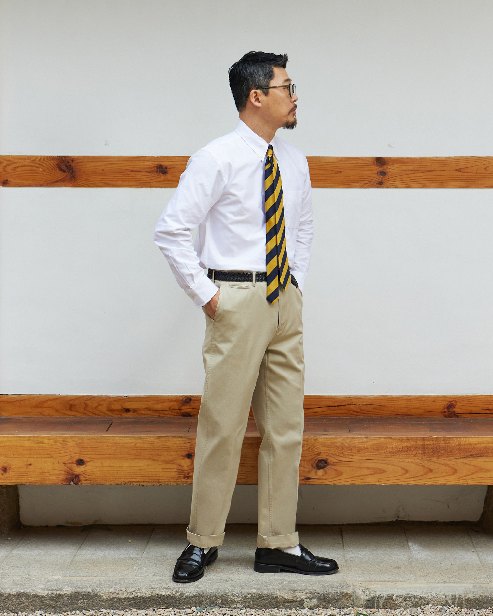 White oxford cloth button-down shirt tucked into khaki chinos with a navy and gold repp tie and penny loafers, worn in a hanok courtyard in Seoul