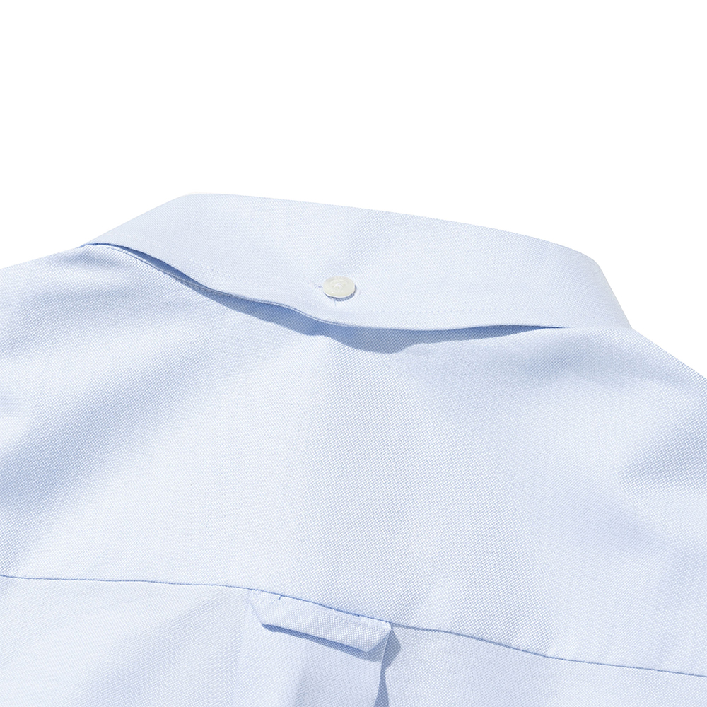 Macro view of the back-collar button on a light blue oxford button-down shirt: a single button at the center back of the collar band above the yoke seam