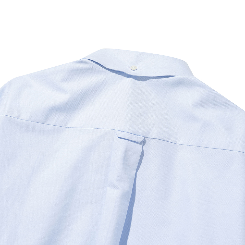 Close-up of the back of a light blue oxford button-down shirt: the yoke seam, the locker loop hanging from it and the box pleat below, with the back-collar button at the top edge