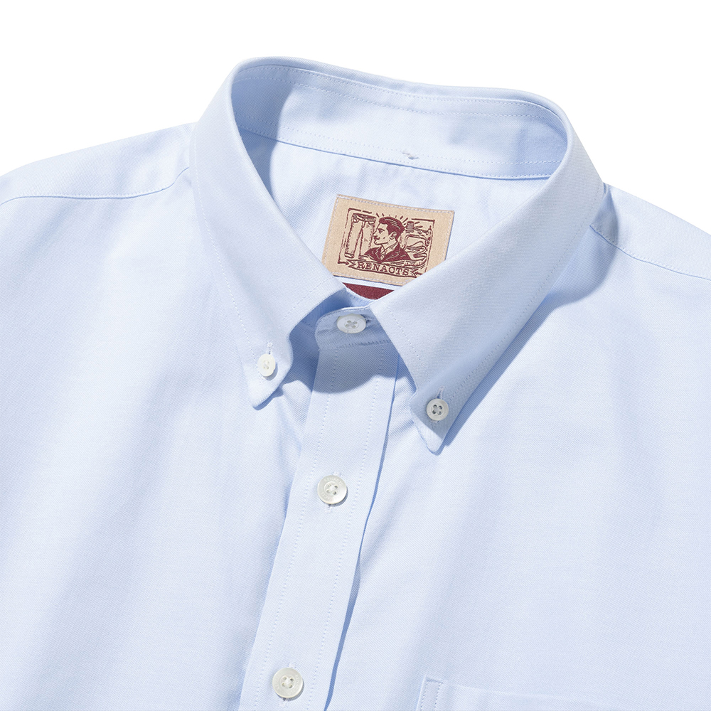 Front collar of a light blue oxford button-down shirt laid flat: buttoned collar points, the top of the placket and the woven label inside the collar band