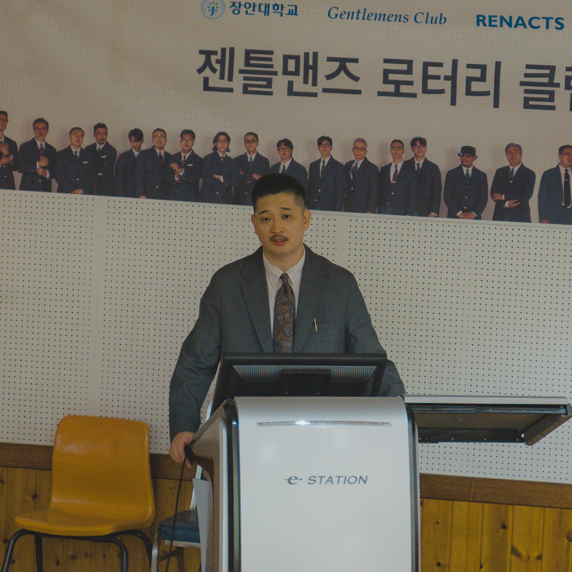 A member in a grey jacket speaking at the lectern.