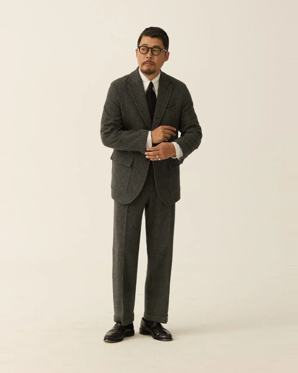 Outfit C: grey herringbone sack cut blazer and matching trousers as a suit, white OCBD, black knit tie, black penny loafers — Renacts FW26 lookbook (in stock)