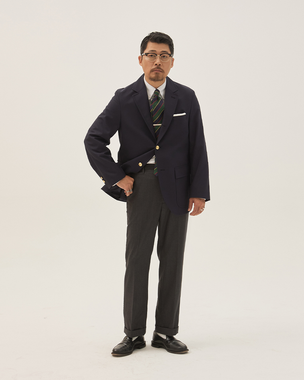 modern ivy tailored register: navy gold-button blazer with natural shoulder, patch pocket and repp stripe tie worn with charcoal herringbone trousers and black penny loafers
