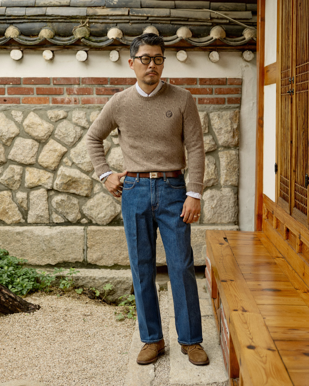 modern ivy relaxed: taupe cable knit crewneck over a striped oxford shirt with wide-leg indigo denim and suede shoes at a Seoul hanok