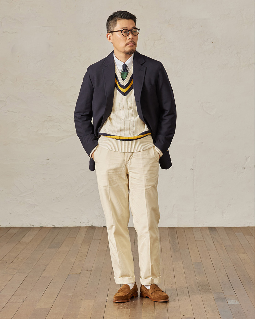 modern ivy layering: navy blazer over a cream cricket V-neck sweater, white shirt and green tie with high-rise cream cotton trousers and brown suede penny loafers