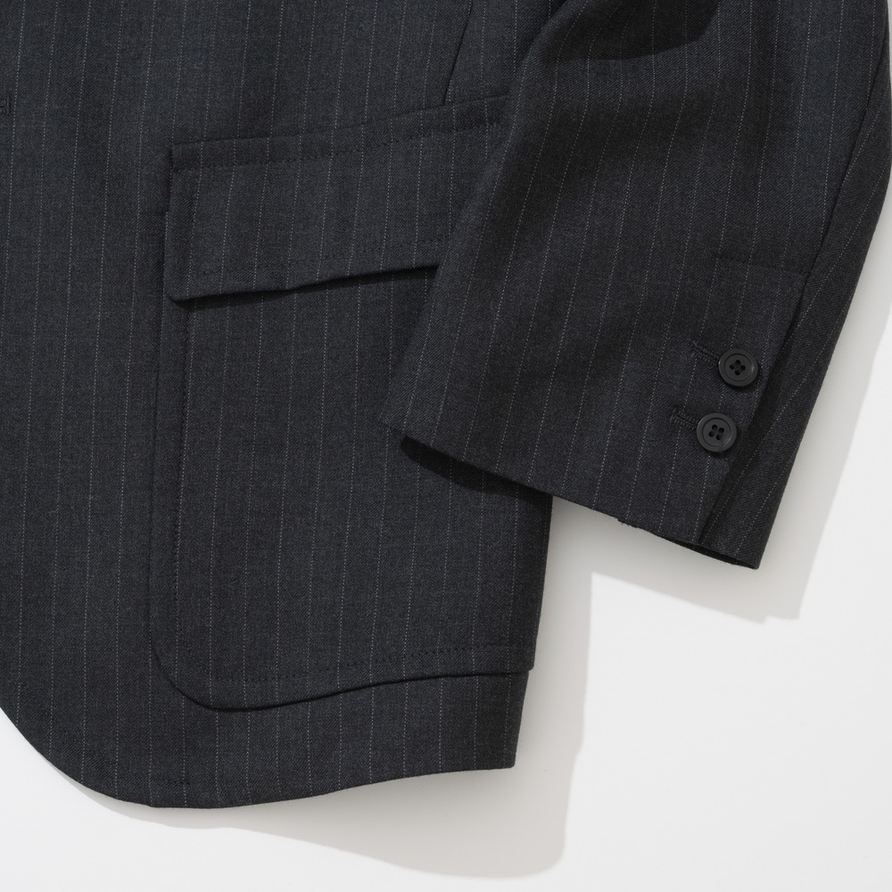 Close-up of a flap patch pocket sewn onto the outside of a charcoal pinstripe sack jacket, with two buttons on the sleeve cuff