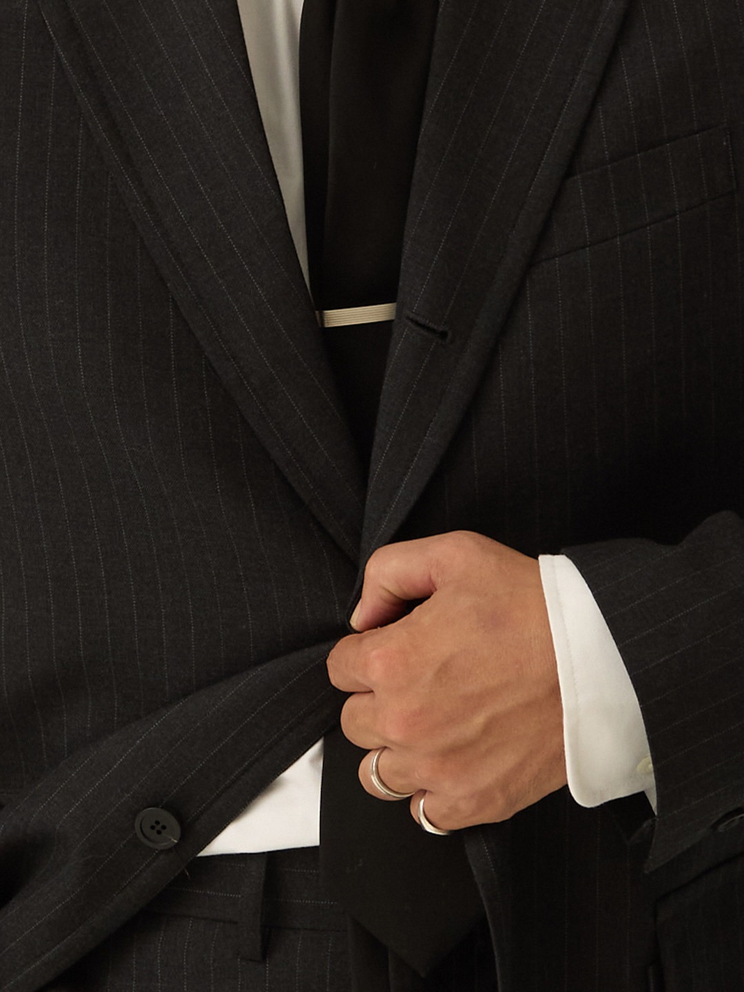 Close-up of a charcoal pinstripe sack jacket being buttoned over a white shirt and a dark tie held by a silver tie bar
