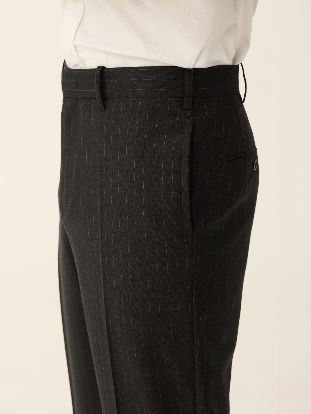 Charcoal pinstripe trousers worn with a tucked-in white shirt and no jacket, showing the flat front and the straight leg