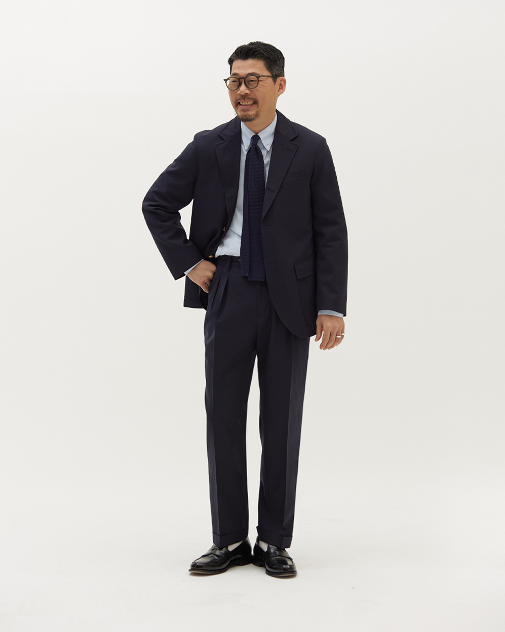 Navy wool trousers worn with a matching navy soft-shouldered blazer, a light blue oxford button-down, a navy knit tie and black penny loafers